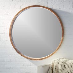 a round mirror hanging on the wall next to a white brick wall and a blanket