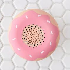 a pink donut with white sprinkles on it sitting on a tile floor