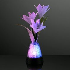 purple flowers are in a blue vase on a black surface with water and sparkles