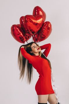 a woman in a red dress is holding several heart shaped balloons on her head and posing for the camera