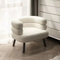 a white chair sitting on top of a hard wood floor next to a dresser and window