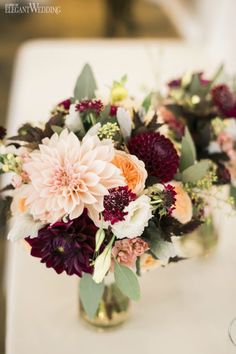 a vase filled with lots of flowers sitting on top of a white table covered in greenery