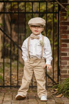 a young boy wearing a bow tie and suspenders standing in front of a gate