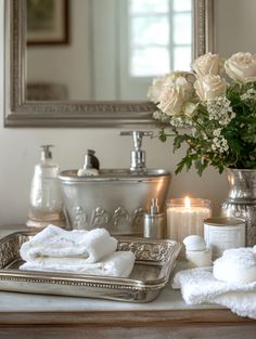 a bathroom with candles, flowers and towels on the counter next to a vase filled with white roses