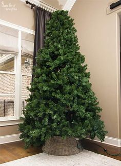 a small christmas tree in a basket on the floor next to a window with curtains