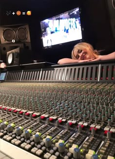 a woman laying down in front of a mixing desk with sound equipment and a television behind her