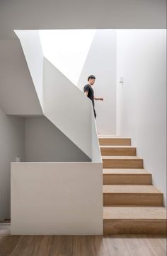 a man standing on the top of some stairs in front of a white wall and wooden floor