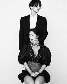 two people sitting on top of each other in front of a white wall with black and white photograph