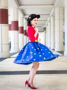 a woman in a red shirt and blue skirt posing for the camera with her hand on her hip