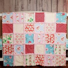 a pink and blue patchwork baby quilt on a wooden floor next to a crib