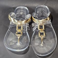 These Flat Clear Sandals Are Perfect For Warm Weather And Boast Cute Golden Bows And T Strap Style Closure Adjustable Round Toe Jelly Sandals, Trendy Gold Sandals For The Beach, Gold Jelly Sandals With Round Toe For Spring, Gold Open Toe Jelly Sandals For Vacation, Gold Open Toe Synthetic Flip Flops, Gold Open Toe Jelly Sandals, Gold Jelly Sandals With Round Toe For Party, Gold Jelly Sandals For Party With Round Toe, Adjustable Gold Synthetic Sandals