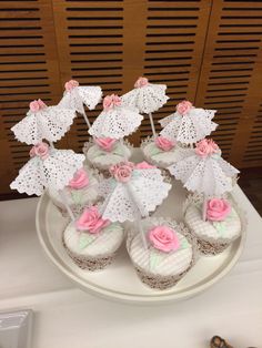 cupcakes decorated with pink roses and umbrellas on a white platter next to scissors