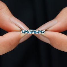 a woman's hand holding a ring with blue stones in it and her fingers