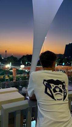 a man sitting on top of a wooden bench next to a tall white building at night