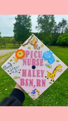 a person holding up a graduation cap with animals and letters on it in the grass