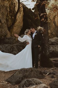 a bride and groom pose for a photo in front of some rocks at their wedding