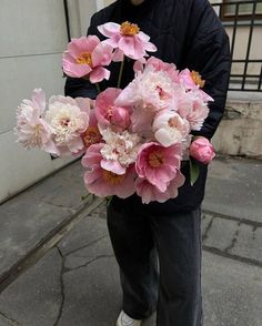 a man holding a bouquet of pink flowers on the street in front of a building