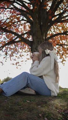 a woman sitting on the ground next to a tree