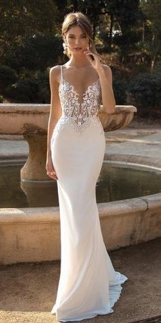 a woman in a white wedding dress standing next to a fountain with her hand on her hip