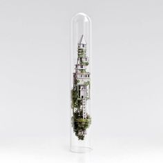 a tall glass tube filled with trees and buildings in the middle, on top of a white surface