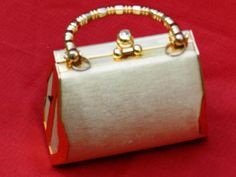 a white and gold purse sitting on top of a red cloth