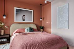 a bedroom with an orange wall and pink bedspread on the bed is shown