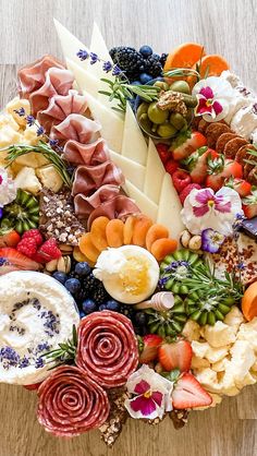 an assortment of cheeses, fruits and meats arranged in a circular arrangement on a wooden surface