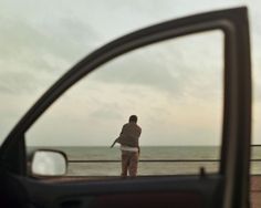 a man standing in front of a car looking out at the ocean