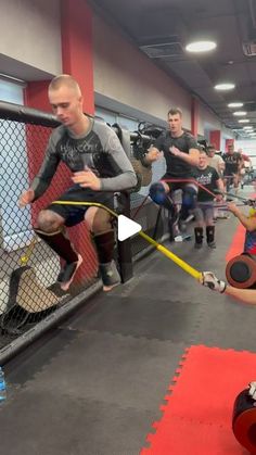 a group of people in a gym with one man holding a barbell and the other woman squatting