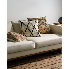 a couch with pillows on top of it in front of a white wall and rug