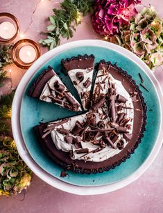 a chocolate pie with white frosting on a blue plate next to candles and flowers