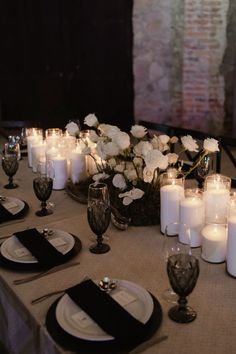 the table is set with white flowers and black napkins, silverware, and candles