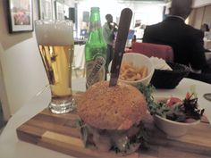 a hamburger and fries on a wooden cutting board with beer in the background at a restaurant