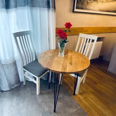 a small table with two chairs next to it and a vase filled with red flowers