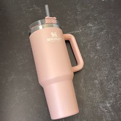 a pink travel mug sitting on top of a black table next to a cup with a straw in it