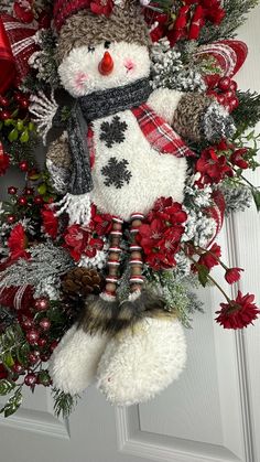 a snowman wreath hanging on the front door with red flowers and pineconis