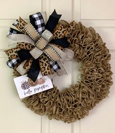 a leopard print wreath with black and white plaid ribbon on the front door, saying hello pumpkin