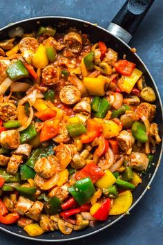 a skillet filled with chicken, peppers and onions on top of a blue surface