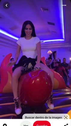 a woman sitting on top of a giant red ball in a room filled with people