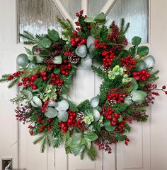 a christmas wreath on the front door with holly, berries and pineconis hanging from it