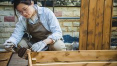 a woman is working on some wood in her yard or garden shed, with one hand holding a piece of wood