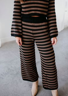 a woman standing in front of a white wall wearing black and brown striped knit pants