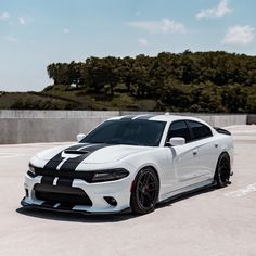 a white dodge charger with black stripes parked in a parking lot next to trees