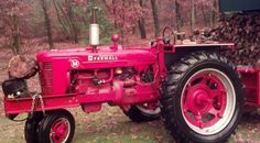 an old red farmall tractor parked in front of a pile of logs and trees