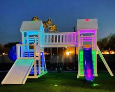 an illuminated play set with slide and slides in the grass at night, lit up by colorful lights