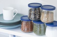 there are many jars with different types of food in them on the shelf next to plates and cups