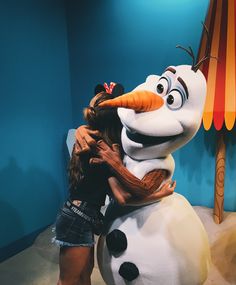 a woman hugging a snowman in front of a blue wall