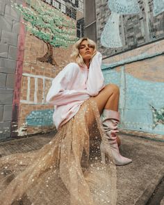 a woman sitting on top of a wooden floor next to a wall covered in graffiti