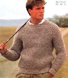 a man holding an umbrella while wearing a sweater and hat in front of a field