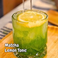 a drink with lemon and ice on a wooden table next to a cutting board that says matcha lemon tonic